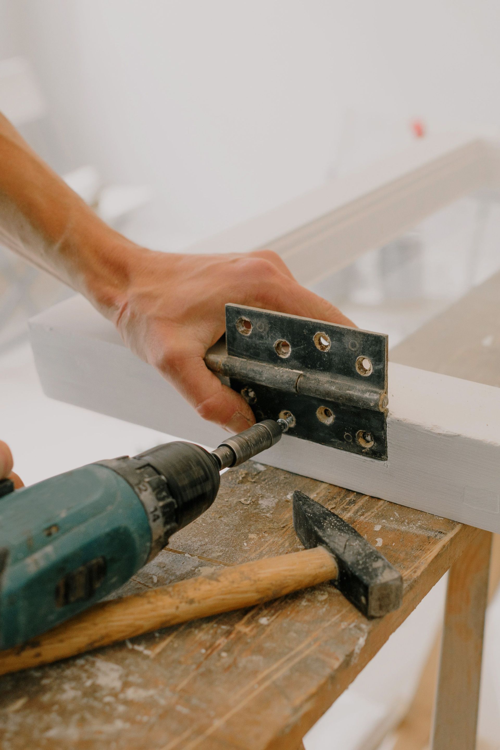 Crop unrecognizable craftsman attaching metal hinge with modern screwdriver on wooden window frame located on wooden board during renovation works